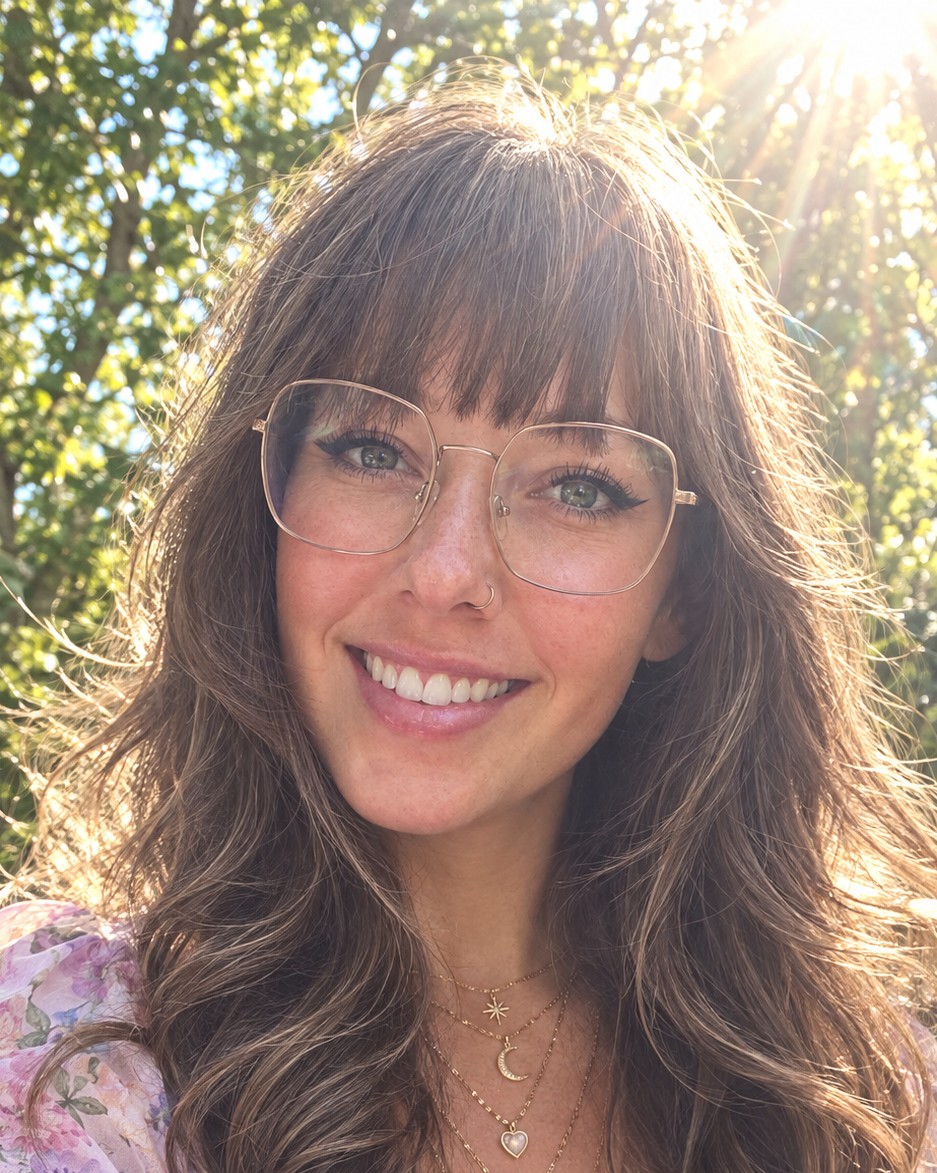 Bri Kelly smiling in a sunlit garden, wearing glasses and a floral dress